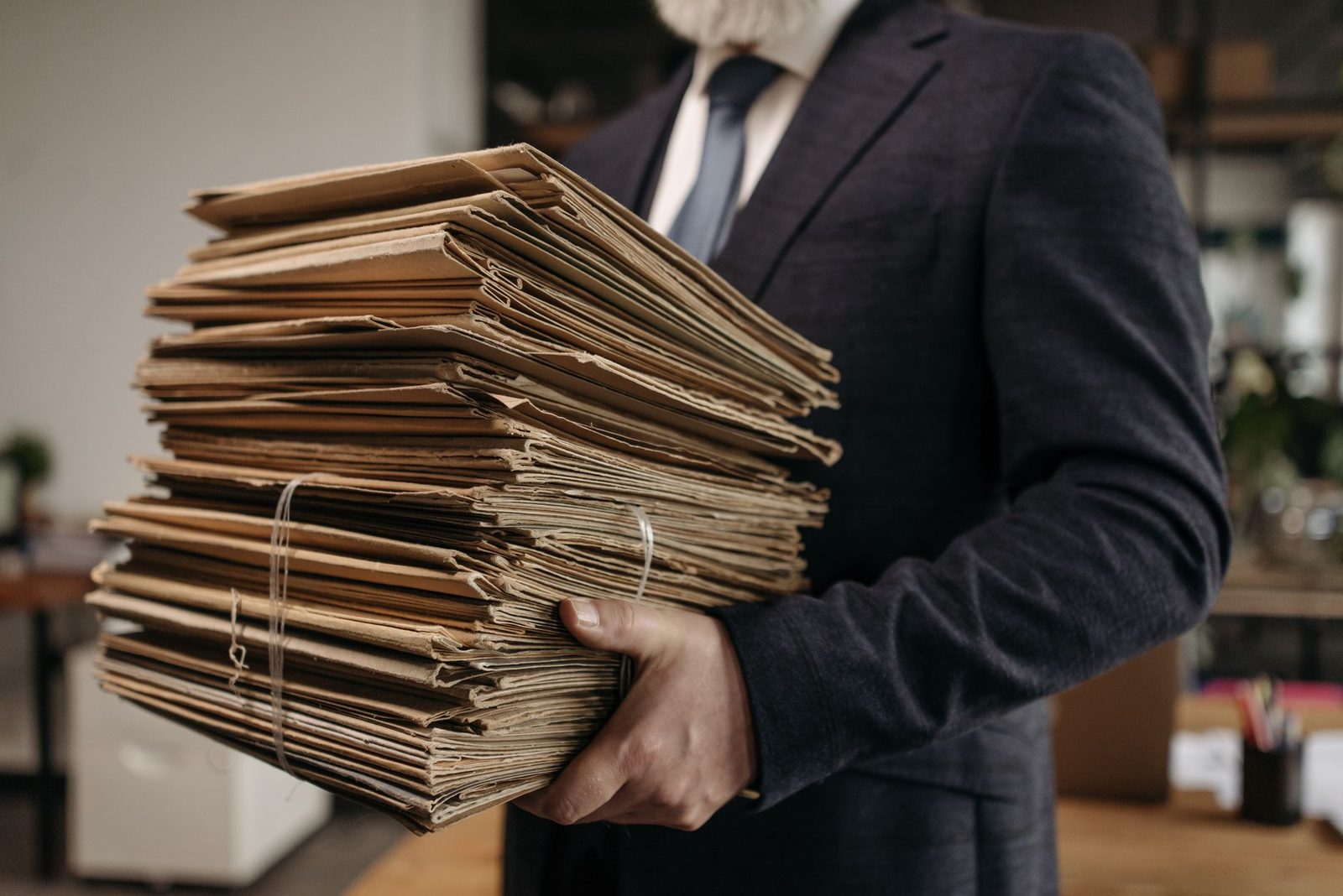 Homme en costume portant une pile de dossiers papier et de chemises cartonnées dans un bureau