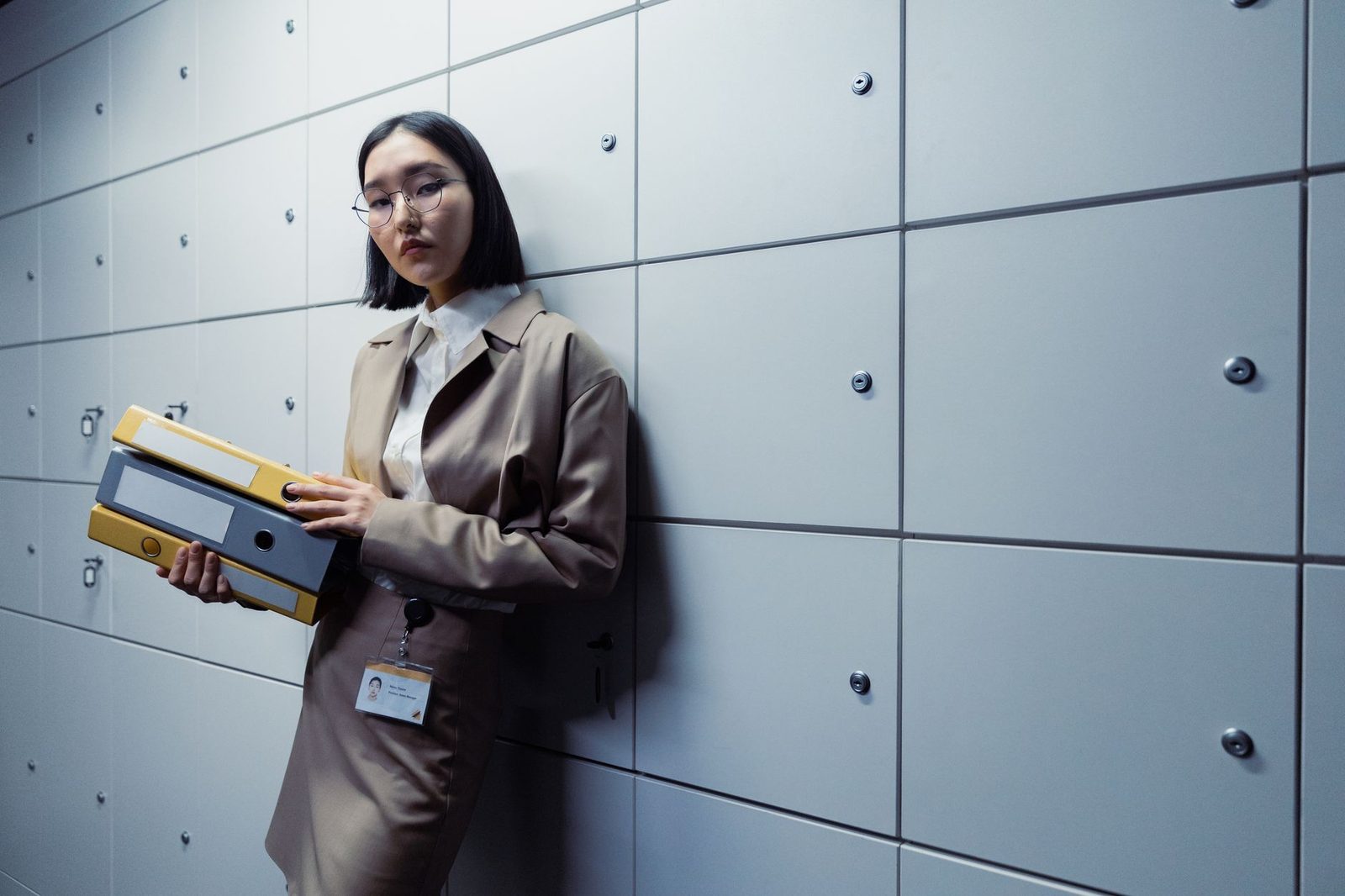 Femme en tailleur portant des classeurs à levier devant un mur d'armoires de rangement métalliques