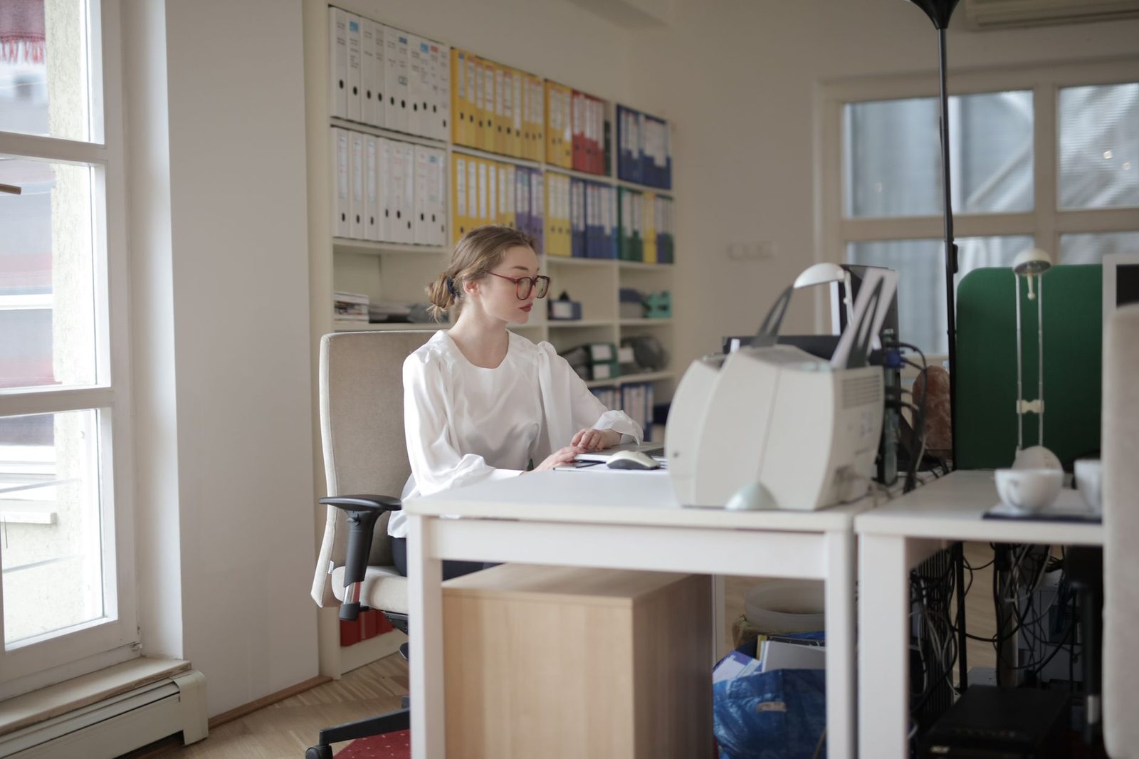 Woman working at a computer in an office with shelves of colourful binders and a scanner