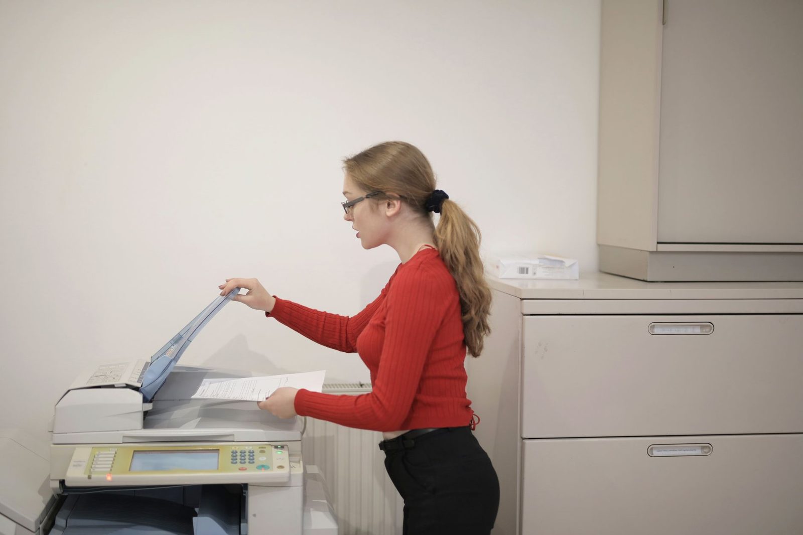 Jeune femme en pull rouge insérant un document dans un photocopieur fax de bureau
