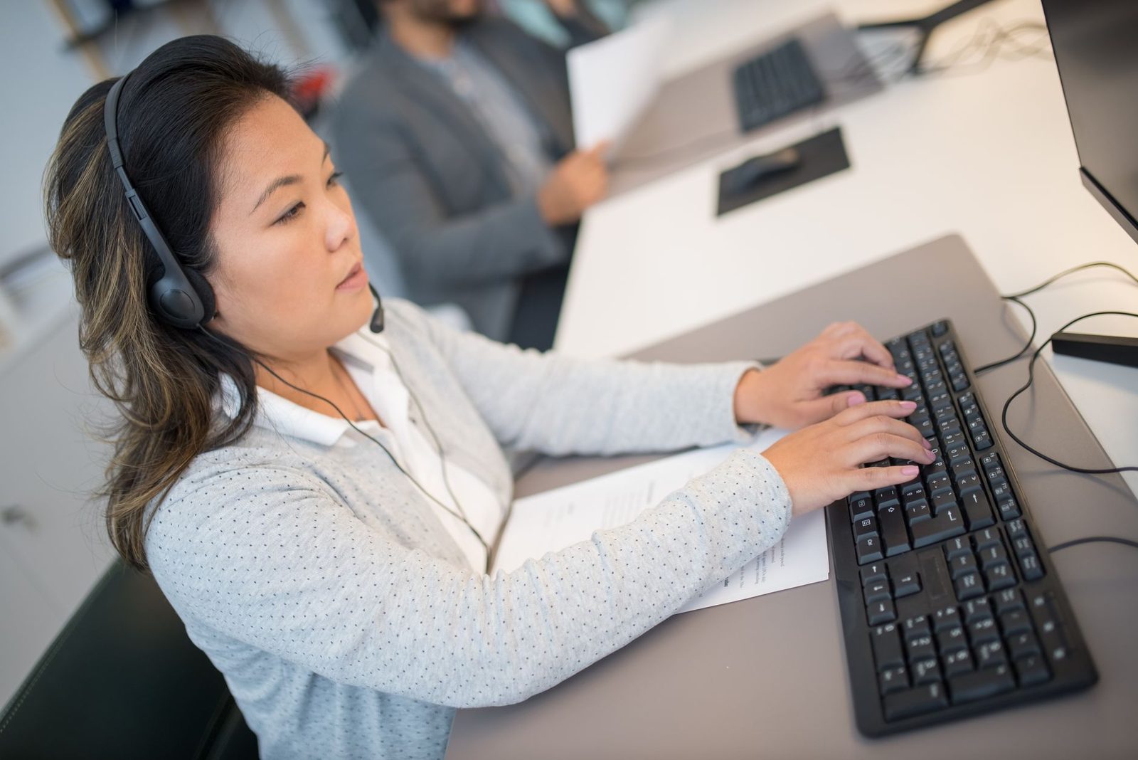 Femme avec casque téléphonique saisissant des informations sur un clavier d'ordinateur dans un bureau