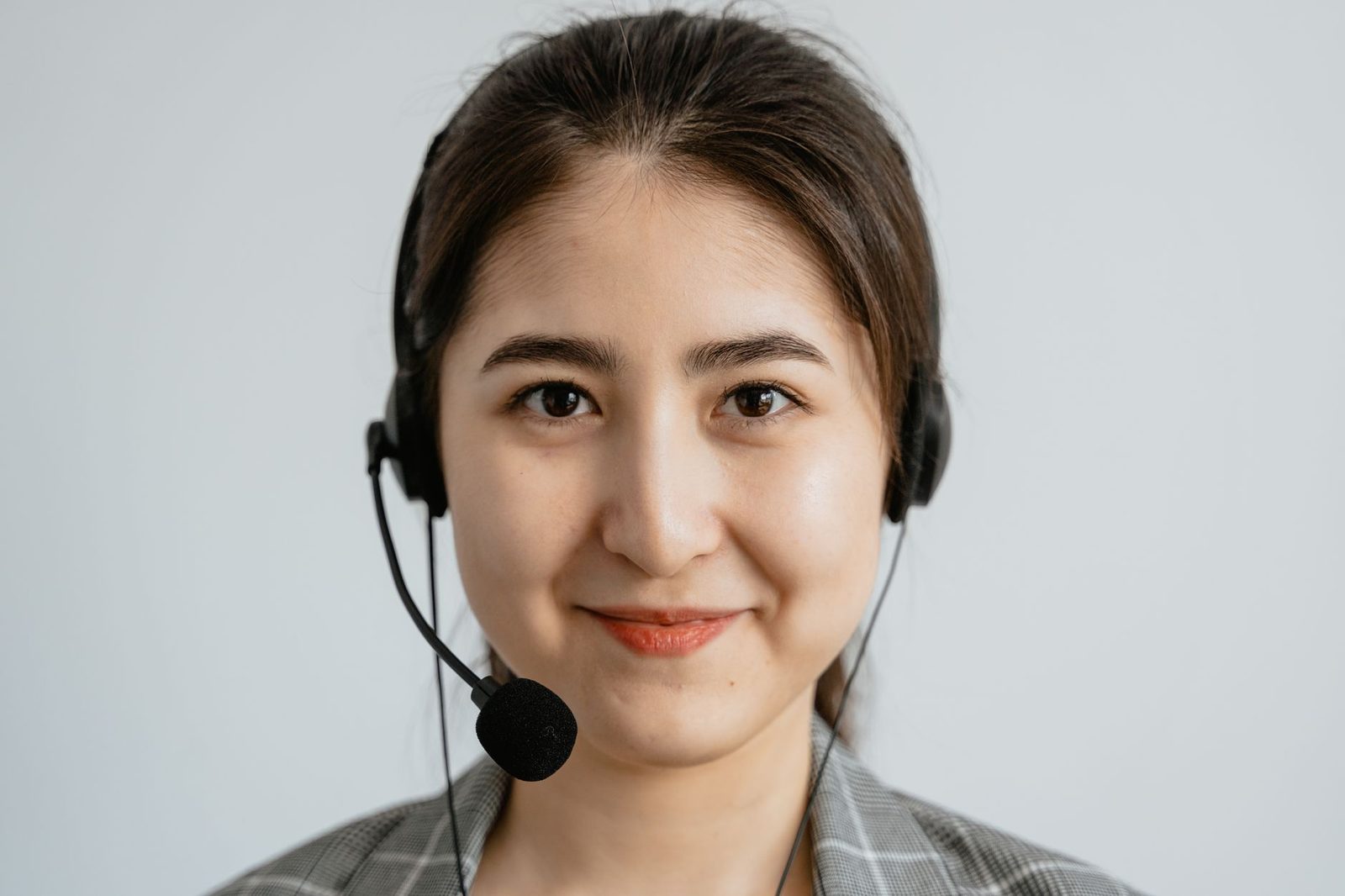 Jeune femme souriante portant un casque-micro, en veste à carreaux, sur fond clair