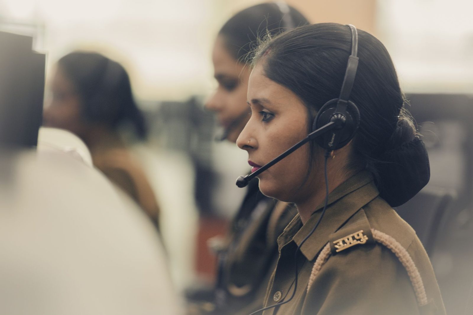 Femme en uniforme portant un casque-micro dans un centre d'appels, collègues en arrière-plan