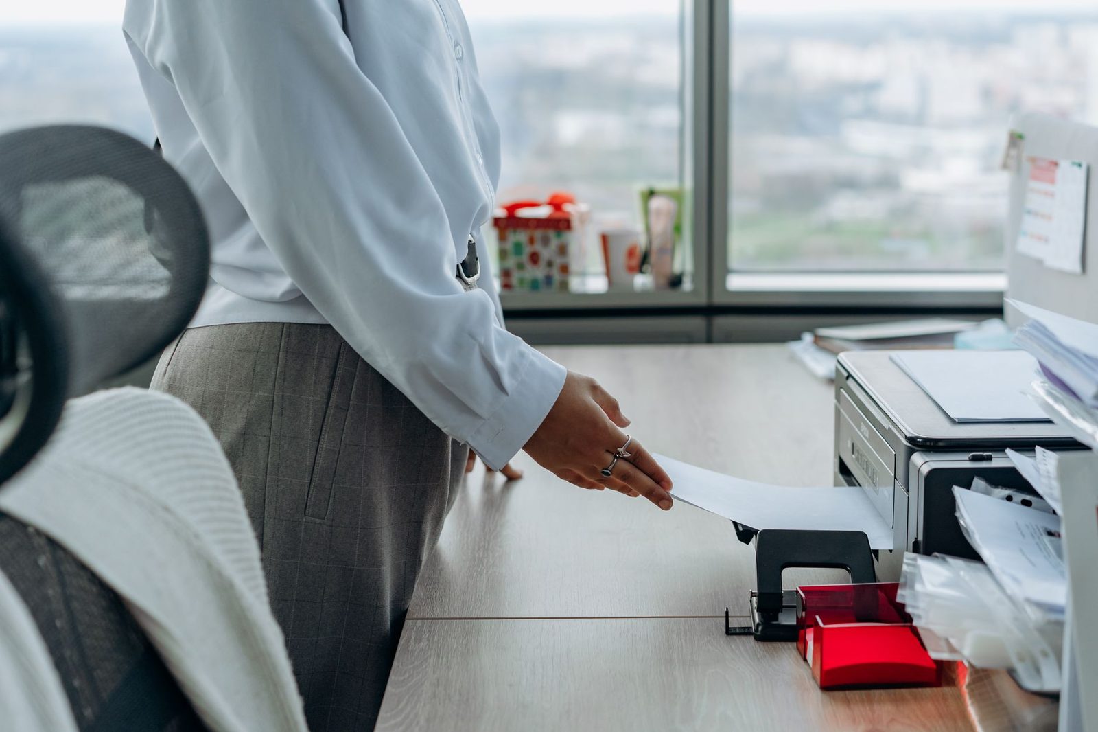 Femme en chemise blanche insérant une feuille de papier dans une imprimante multifonction au bureau