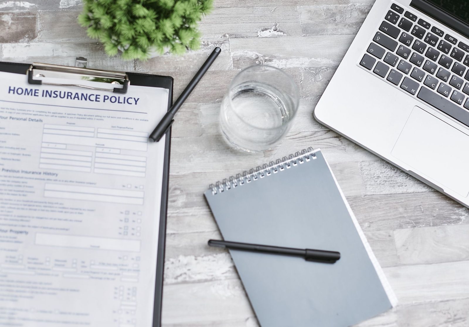 Administrative form on a clipboard, pen, notepad, glass of water and laptop on a desk
