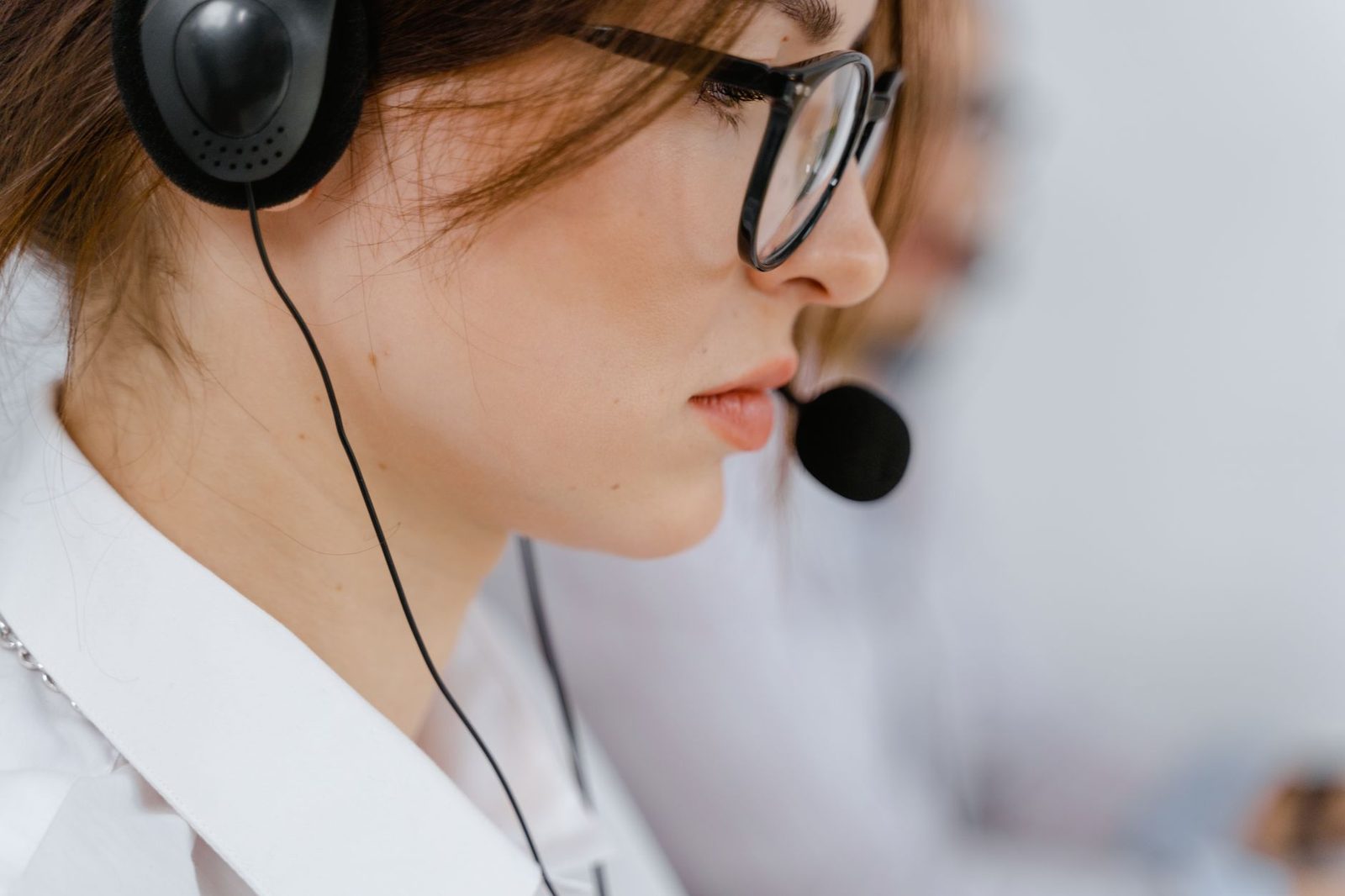 Femme avec lunettes et casque-micro au téléphone dans un centre d'appels, collègue en arrière-plan