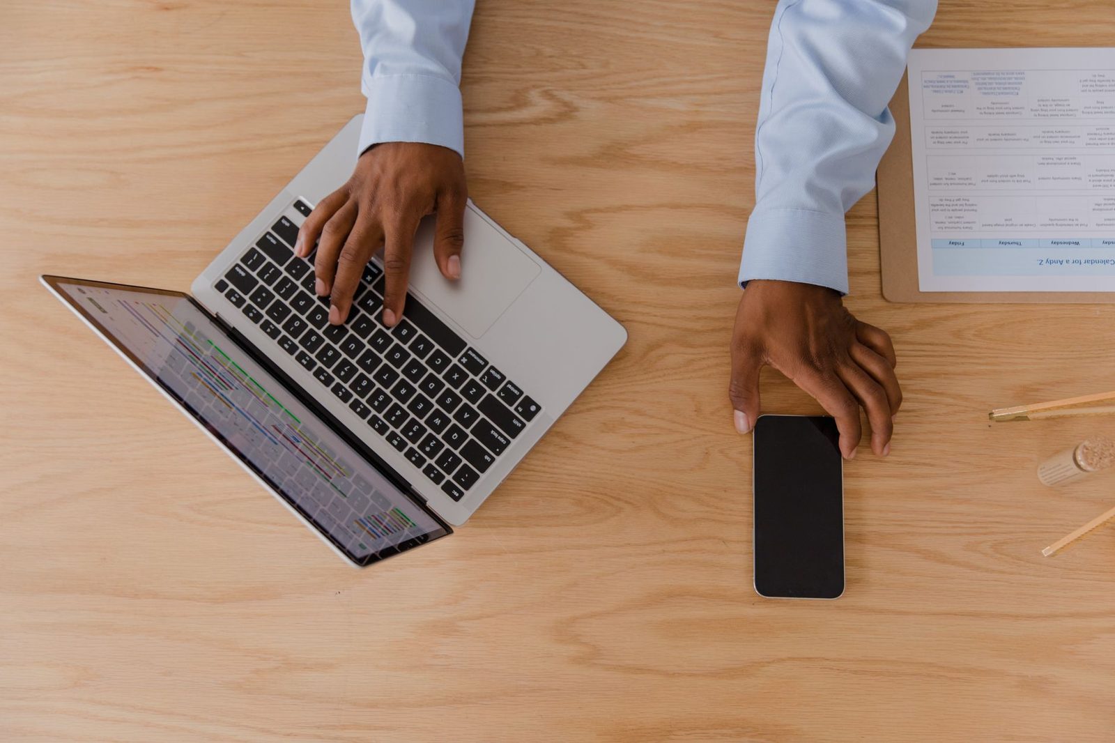 Vue de dessus d'une personne utilisant un ordinateur portable et un smartphone sur un bureau en bois.