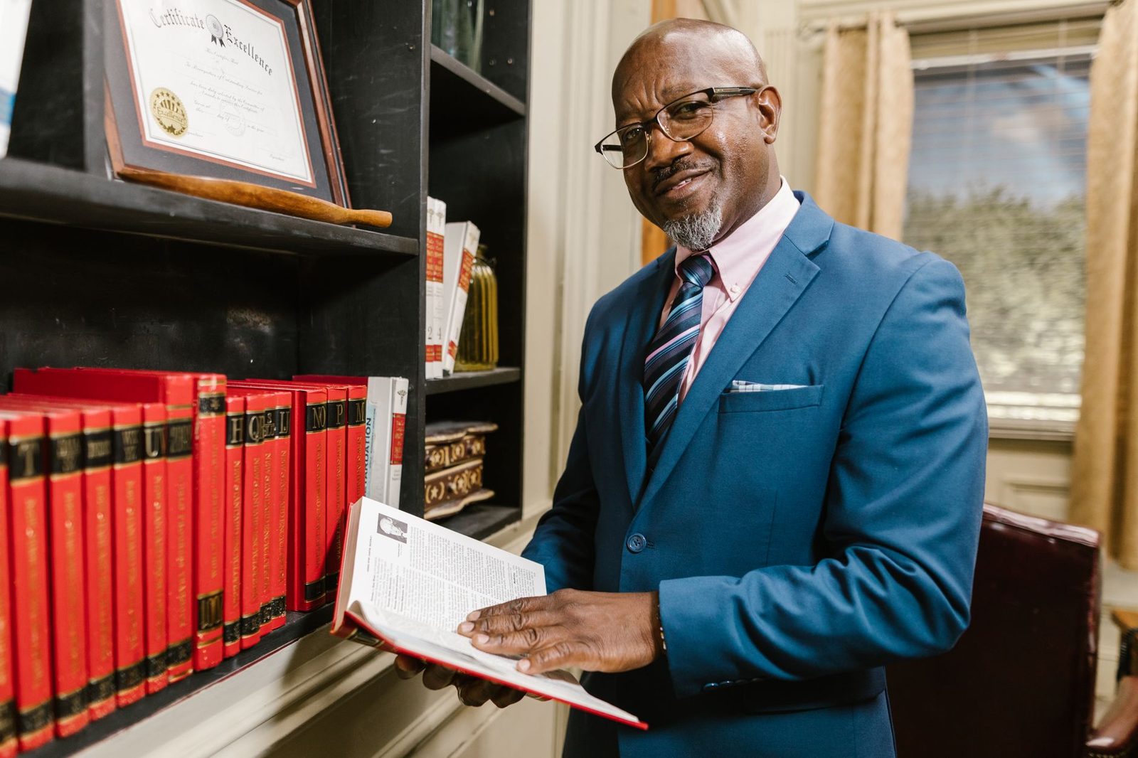 Homme en costume bleu consultant un ouvrage devant une bibliothèque de codes juridiques rouges
