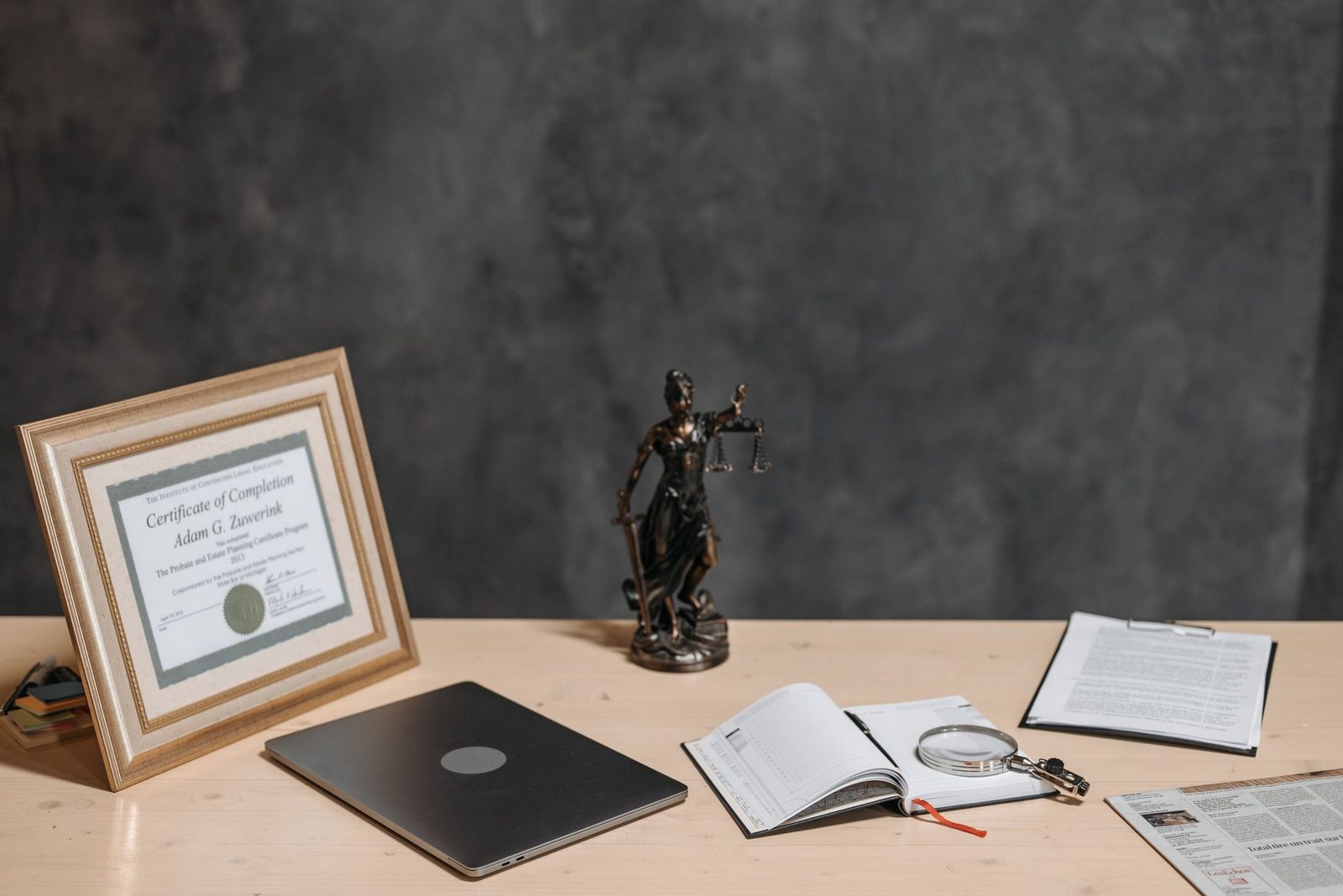 Bureau juridique avec ordinateur portable, statuette de la justice, livre ouvert, loupe et certificat encadré