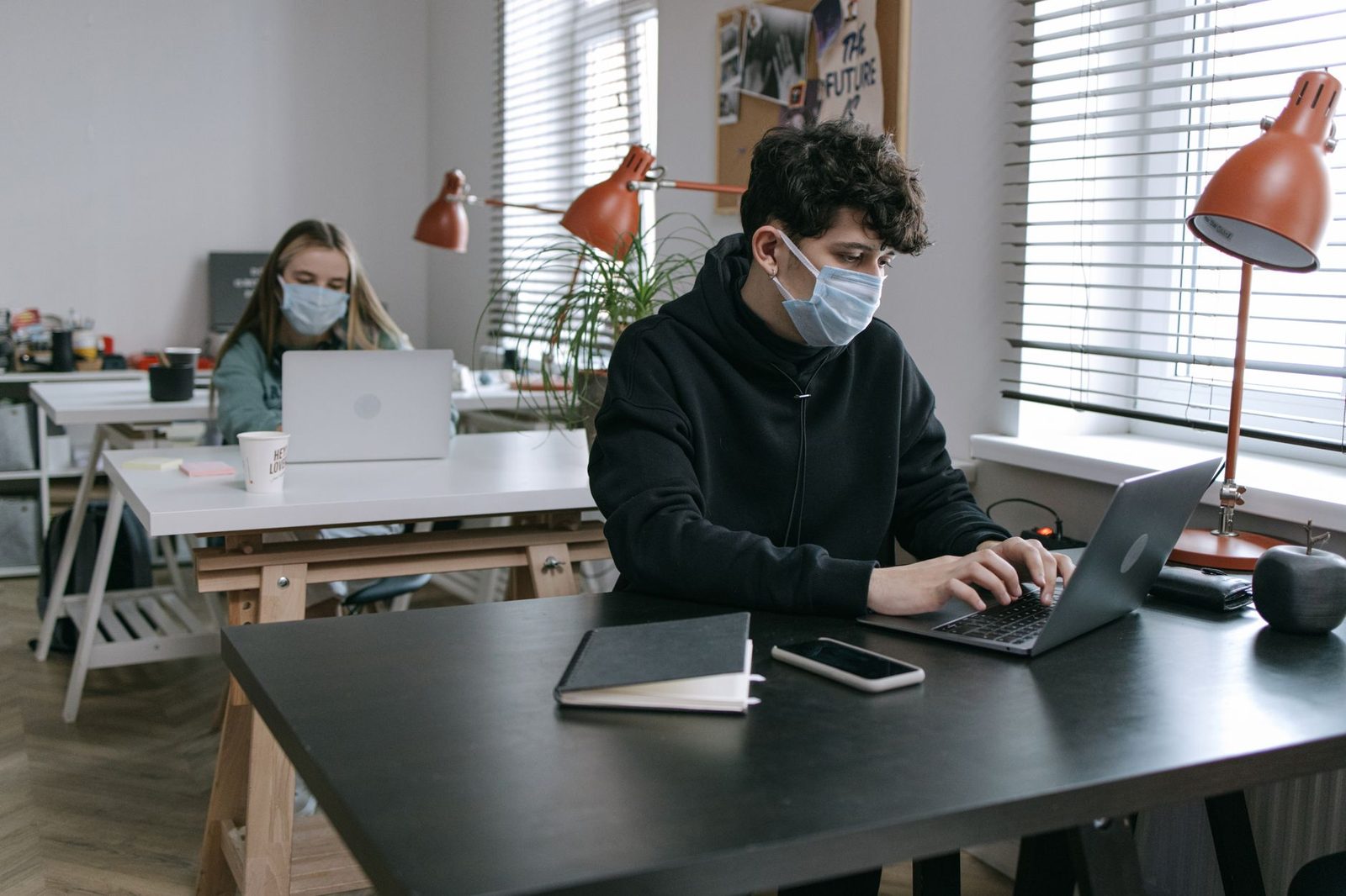 Deux personnes portant un masque chirurgical travaillent sur des ordinateurs portables dans un bureau