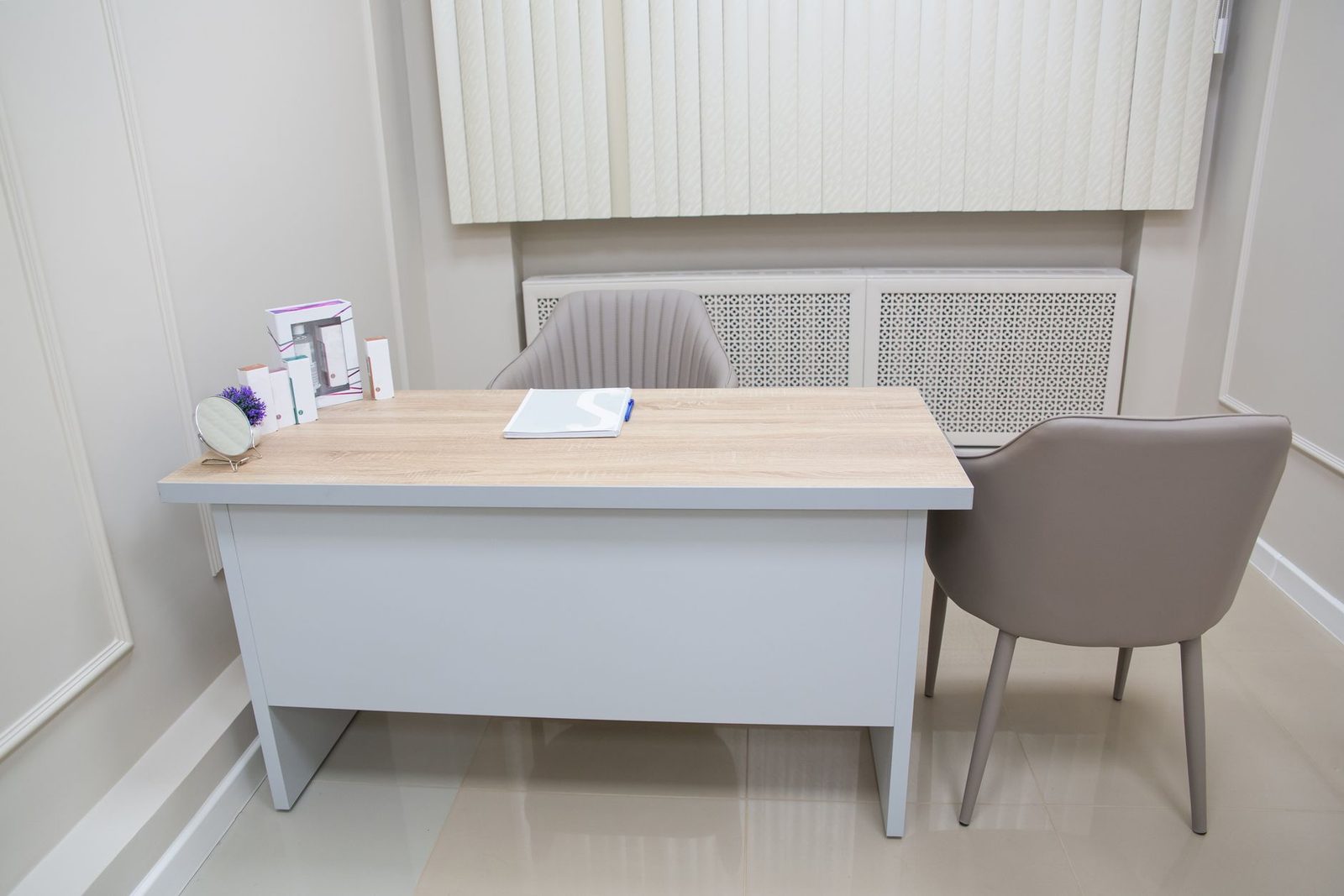 Bureau de consultation médicale avec table en bois clair, cahier ouvert et deux fauteuils gris