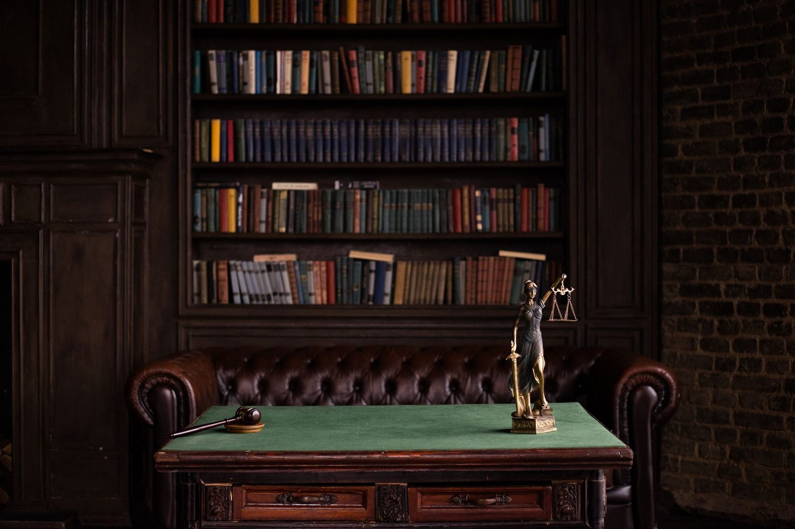 Statuette de la justice et marteau sur un bureau à tapis vert devant une bibliothèque de livres de droit