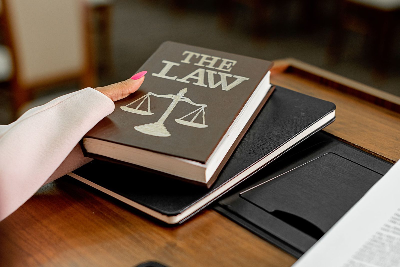 Main posée sur un livre de droit orné d'une balance, posé sur un carnet noir, sur un bureau en bois