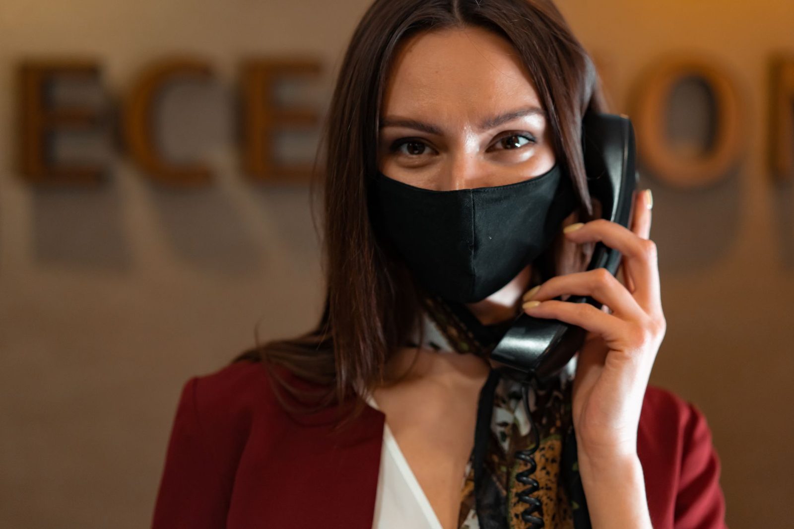 Femme portant un masque noir à l'accueil, téléphonant avec un combiné fixe