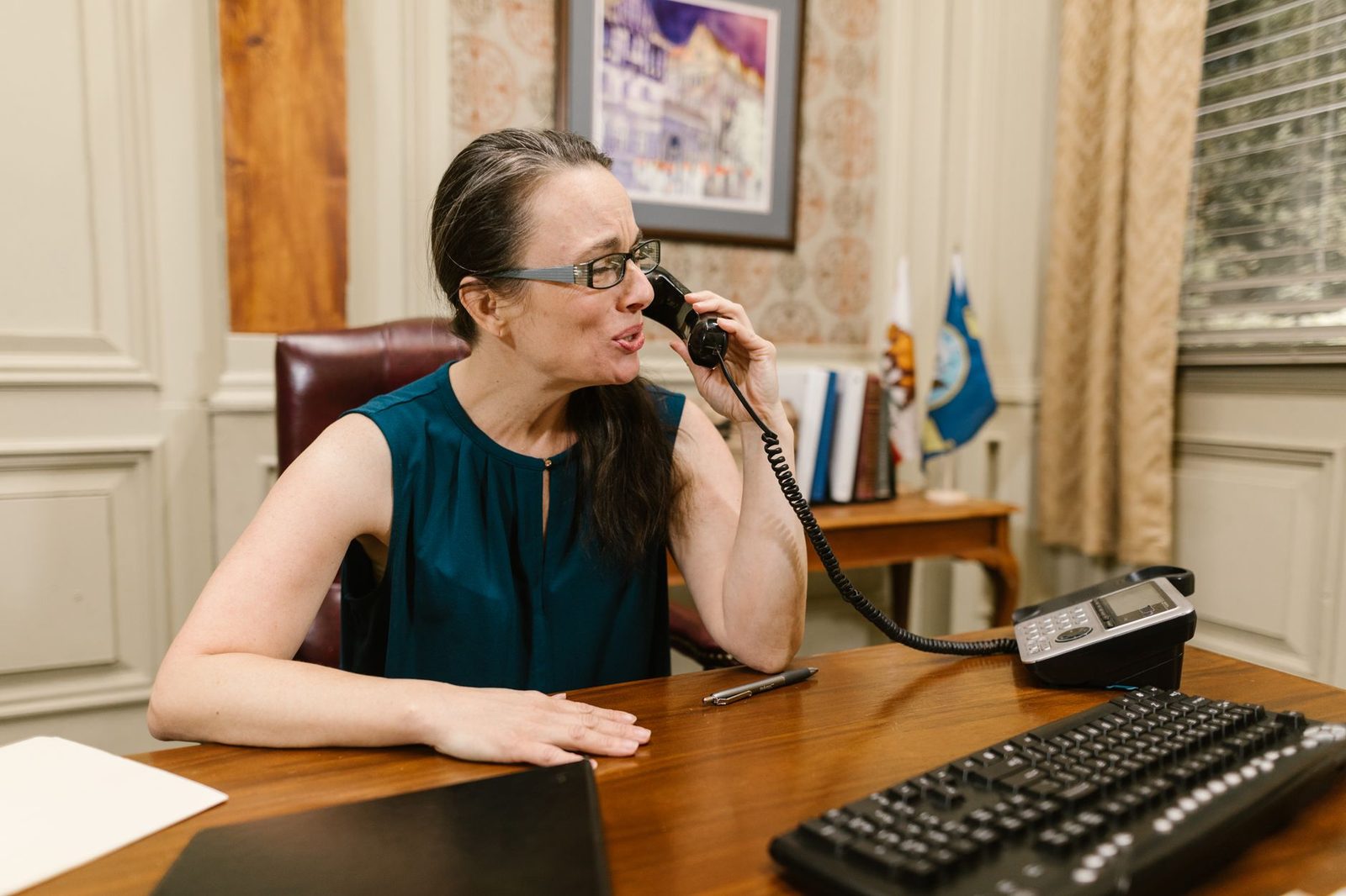 Femme à lunettes au téléphone fixe derrière un bureau avec clavier et documents