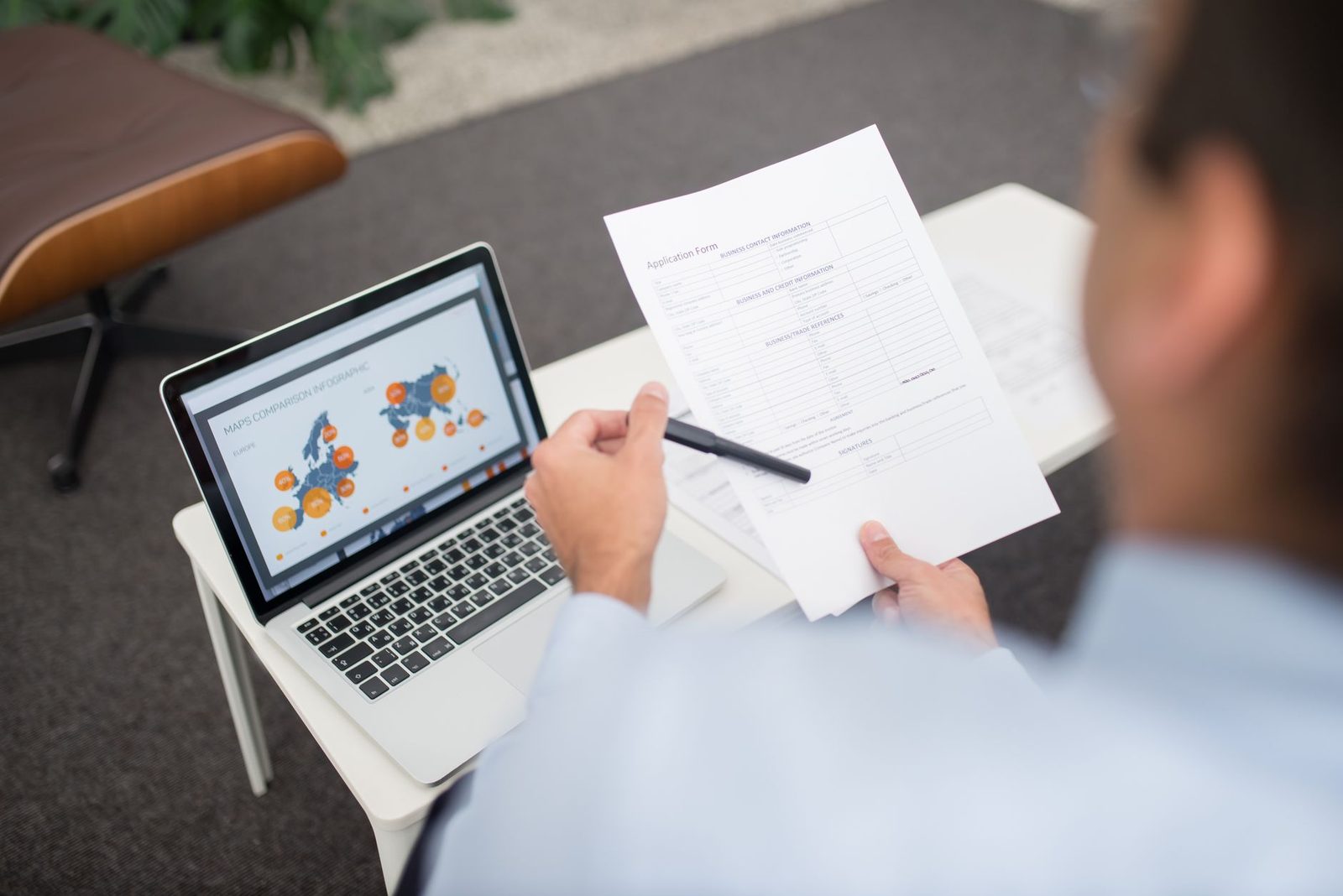 Homme en chemise remplissant un formulaire papier avec un stylo devant un ordinateur portable ouvert