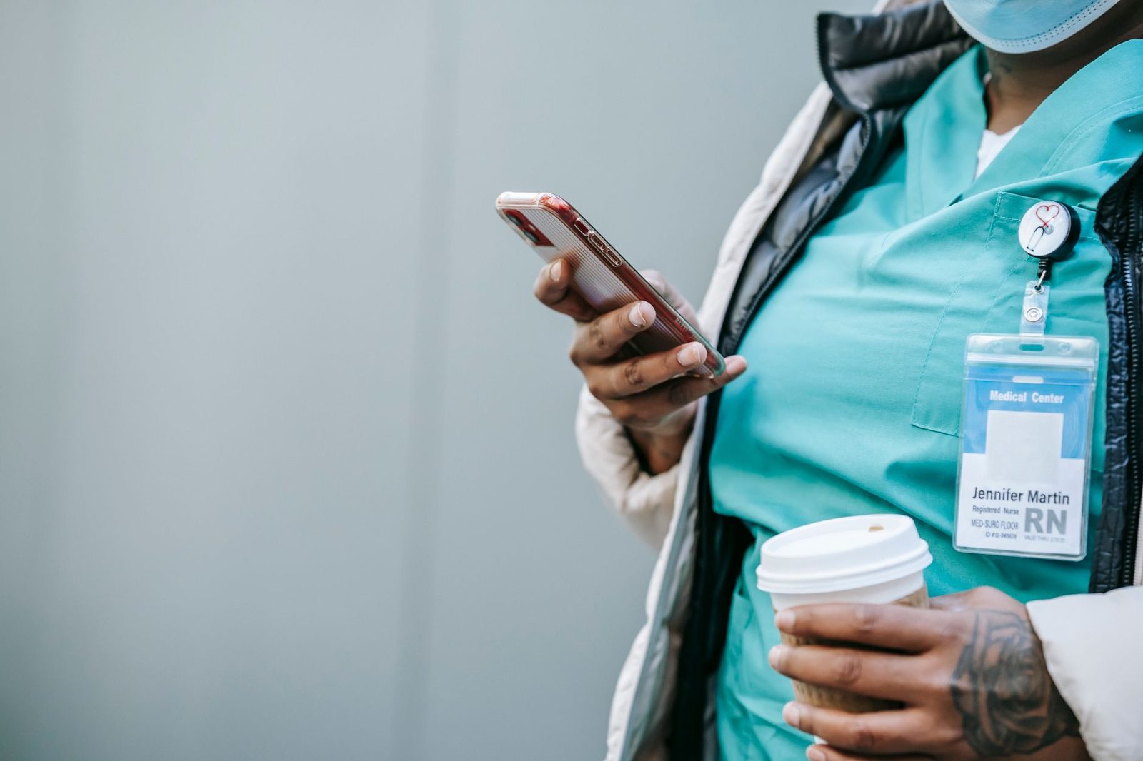 Soignante en tenue médicale avec badge consultant son smartphone, un gobelet de café à la main