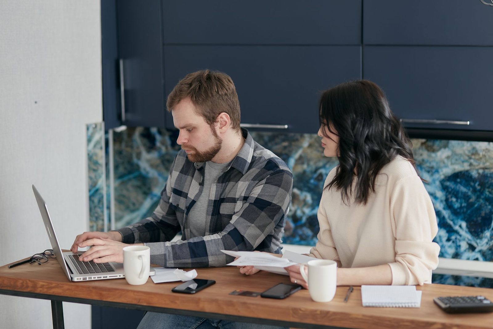 Un homme sur un ordinateur portable et une femme tenant des documents papier à une table de bureau