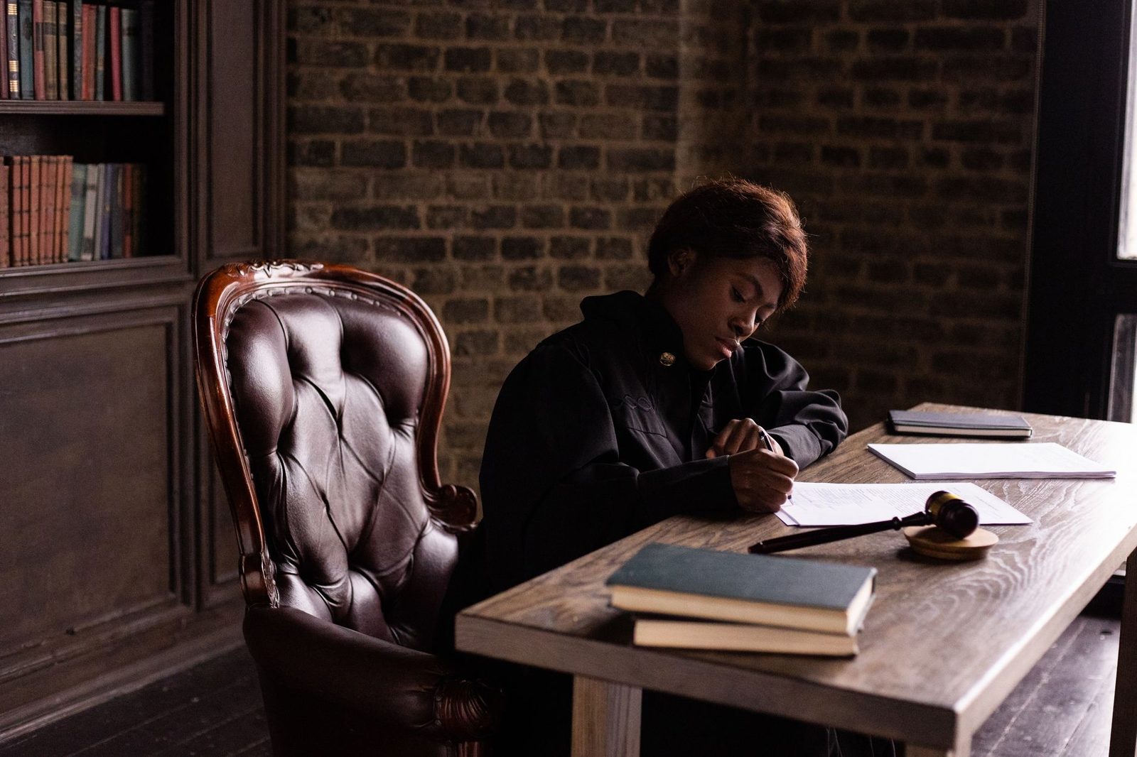 Femme en robe noire écrivant sur des documents à un bureau en bois avec maillet de juge et livres