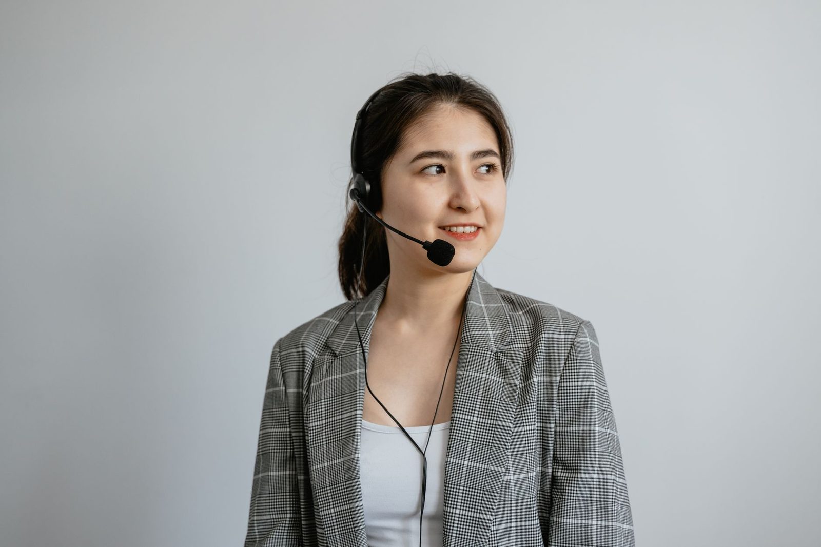 Young woman in a checked jacket wearing a call-centre headset against a light grey background