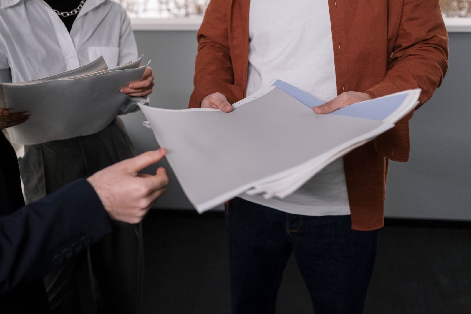 Three people standing and exchanging bundles of paper documents and a file folder in an office