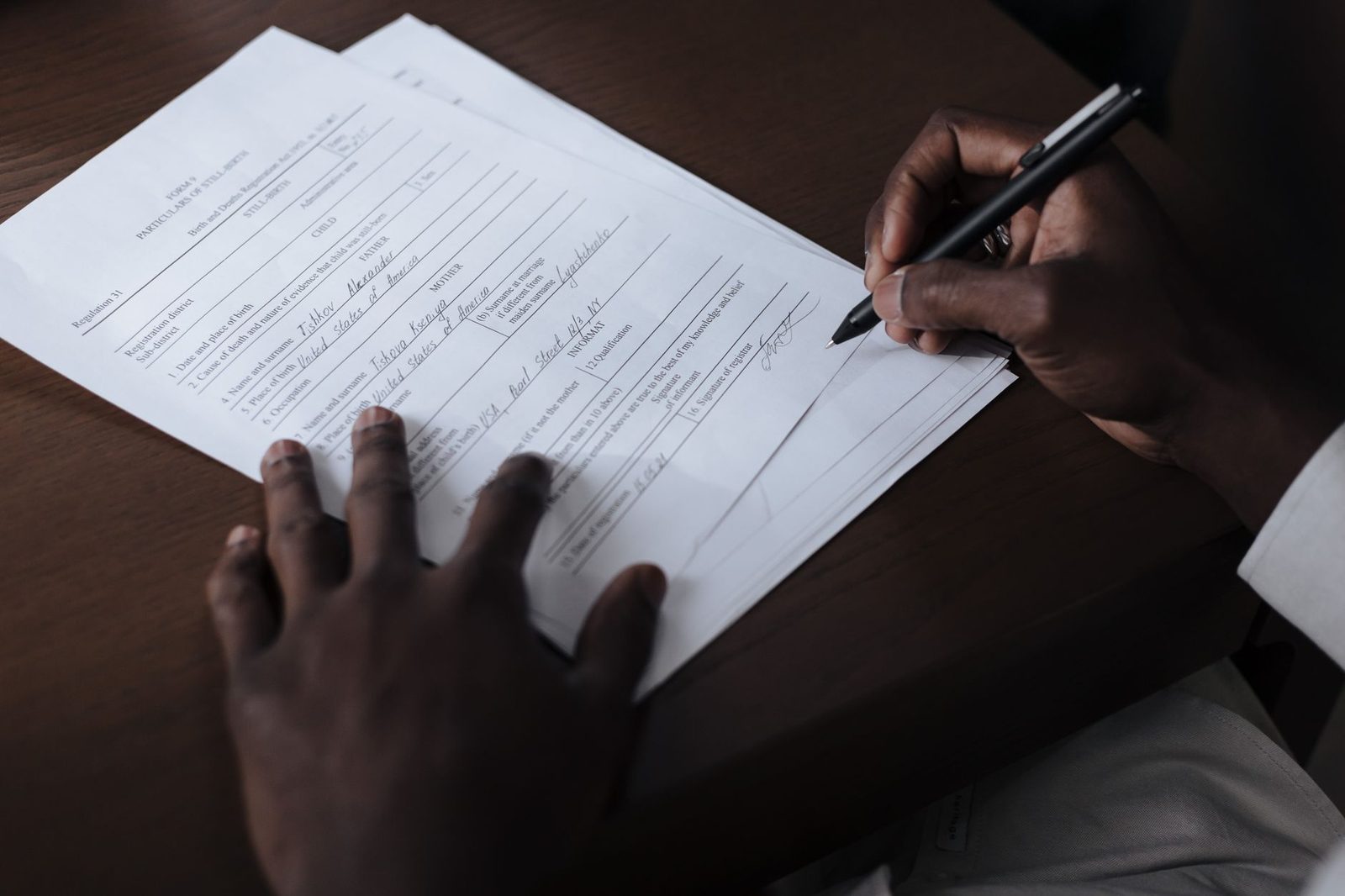 Mains d'une personne remplissant et signant un formulaire administratif au stylo sur un bureau en bois