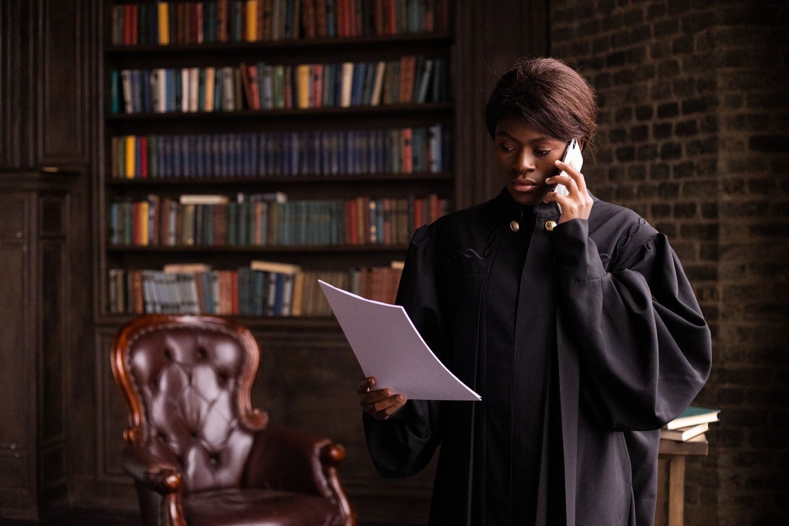 Femme en robe d'avocat lisant un document et téléphonant devant une bibliothèque juridique