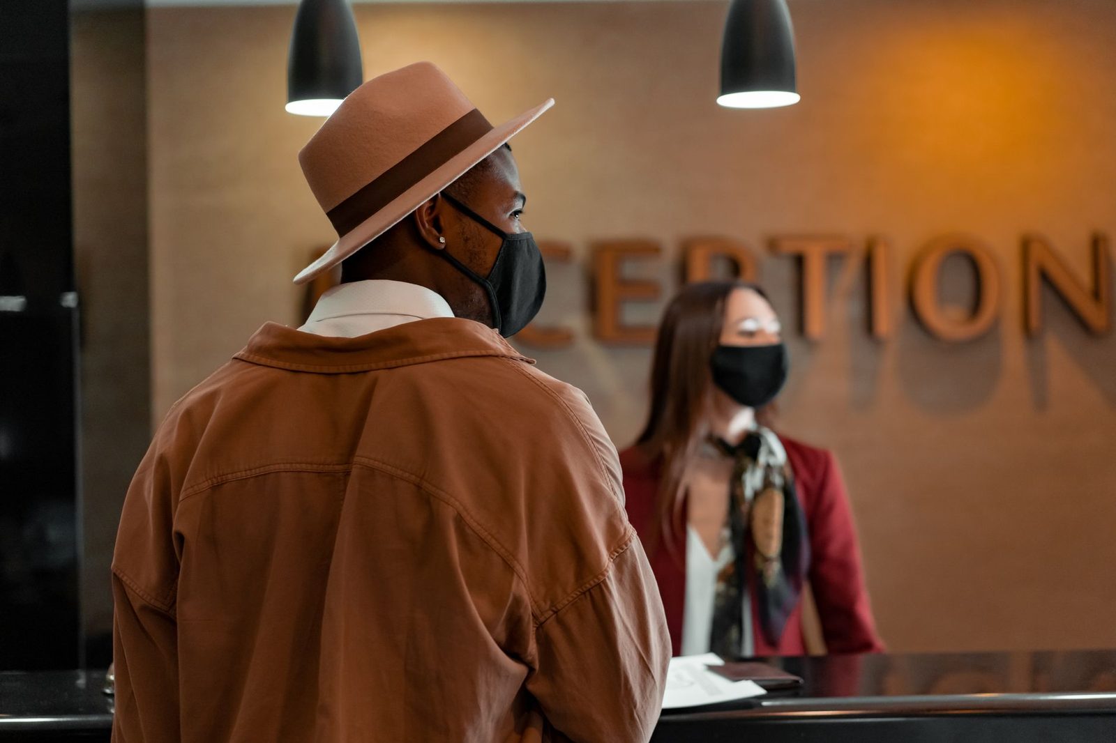 Man in a hat and mask at a reception counter being served by a masked employee